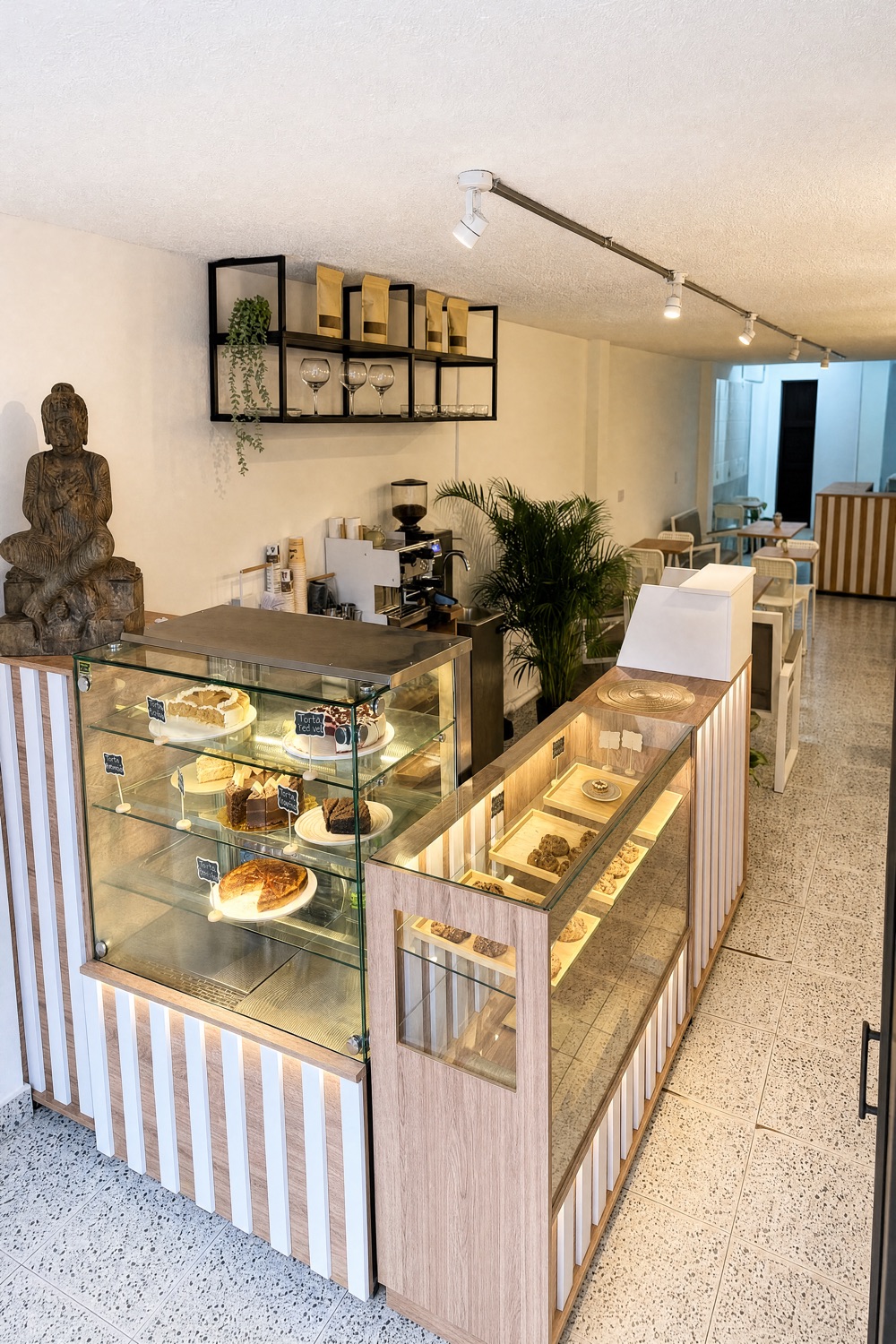 Interior de Le Morita: vitrina de pasteles, plantas y un buda de piedra